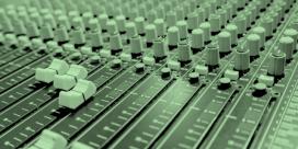 A monochrome photo of a mixing console very close up showing some sliders and knobs. the image is tinted a light green.